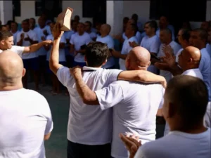 Restauração e Esperança: O Impacto Humano do Projeto Renascer Dois homens se abraçando durante culto do Projeto Renascer na Penitenciária de Parnaíba, um deles levantando a Bíblia em sinal de vitória.